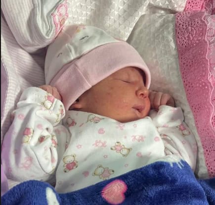 Newborn baby peacefully sleeping, wrapped in a blanket, wearing a pink hat, in a hospital setting.